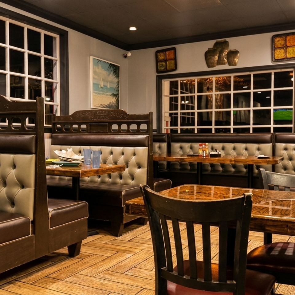 Empty restaurant dining room with dark booths, wooden tables, and large windows.